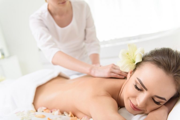 Professional masseuse is standing and massaging female back. Woman is lying and smiling with relaxation